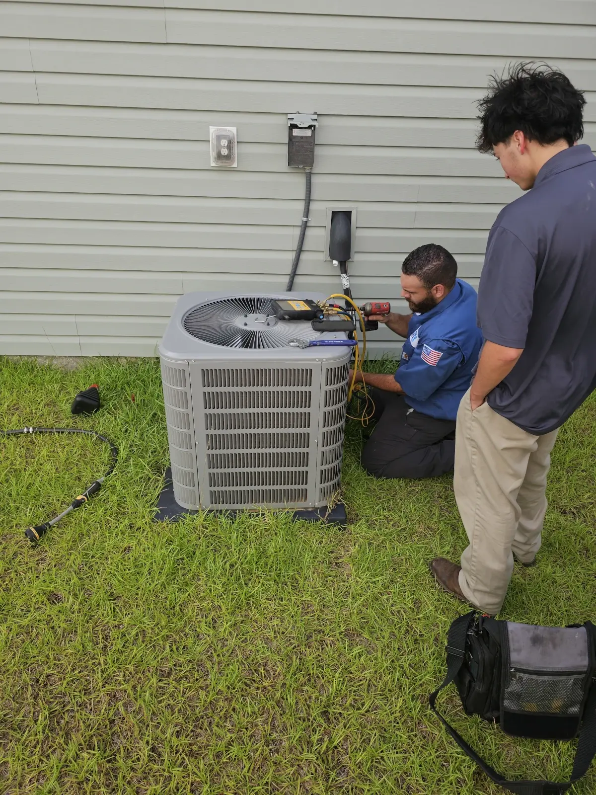 HVAC technician testing an outdoor AC unit while another technician observes.