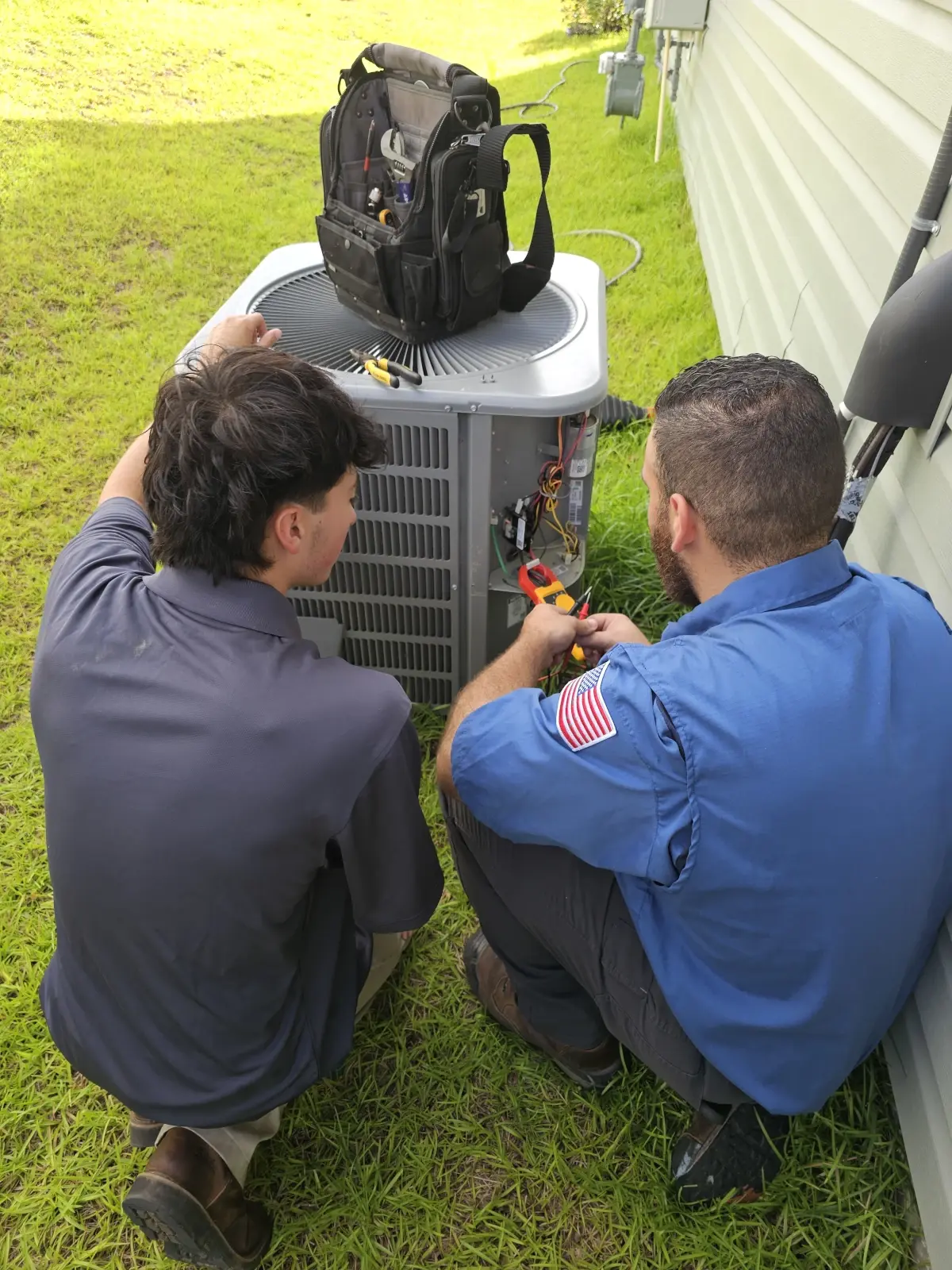 Two HVAC technicians inspecting and repairing an outdoor air conditioning unit.