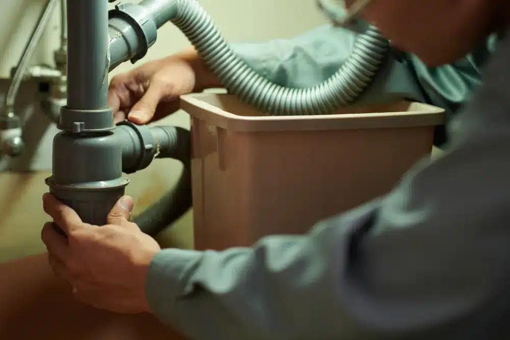 Emergency drain cleaning services in Columbia, SC - Home service worker cleaning plastic pipe under kitchen sink